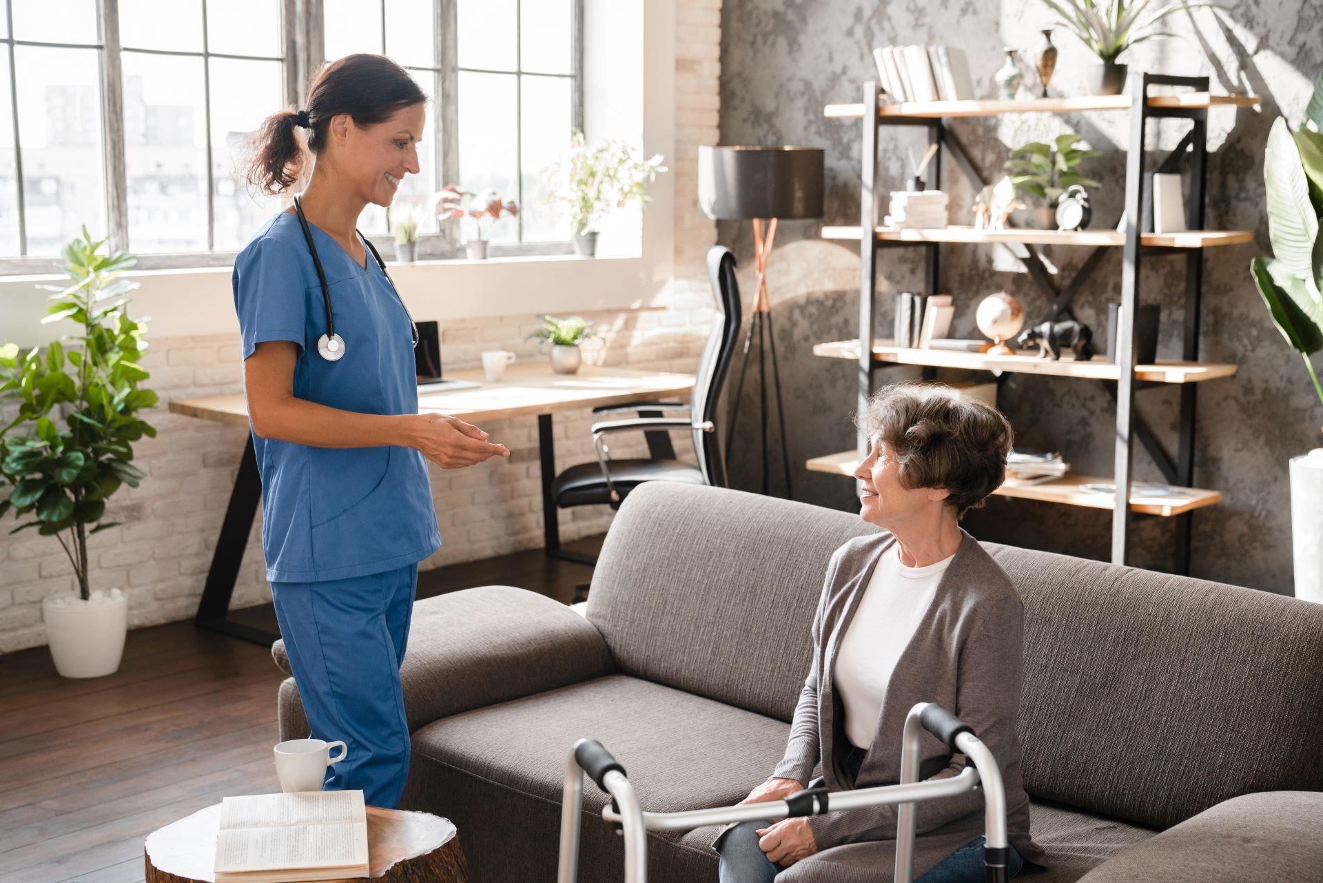 Pflegekraft spricht mit älterer Frau im Wohnzimmer.